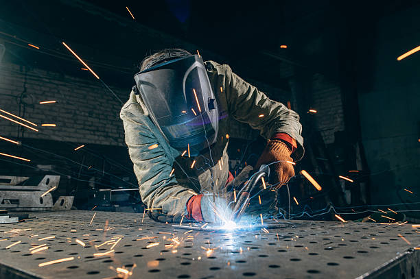 A professional metal worker welds steel in an industrial workshop, wearing protective gear as bright sparks fly from the welding process.